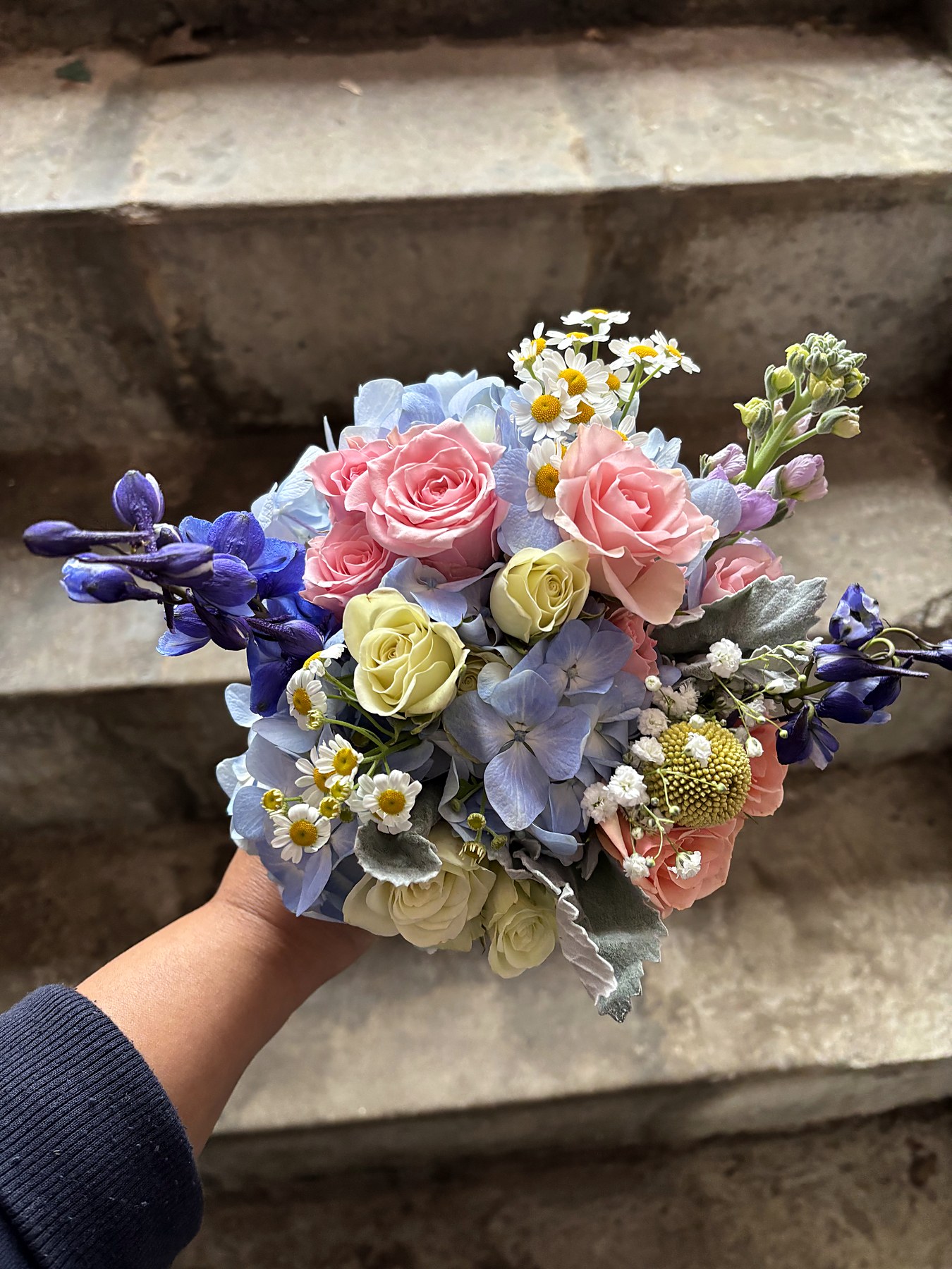 Pastel bridal bouquet with pink roses, blue hydrangea, delphinium, and daisies