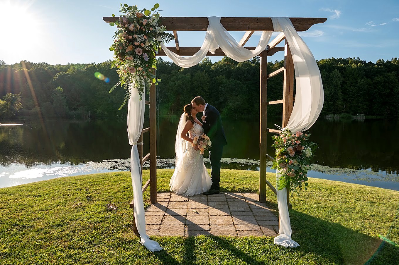 Bride and groom kissing under a floral arch at a lakeside ceremony